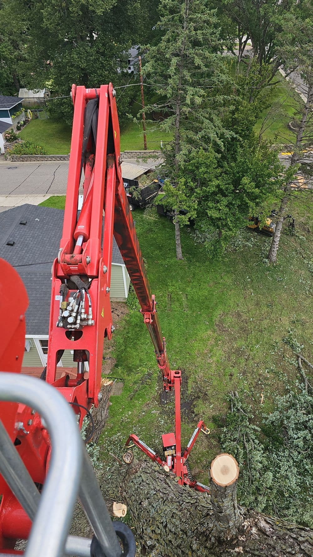 High view of a cherry picker used for tree removal, showcasing trees and residential area below.