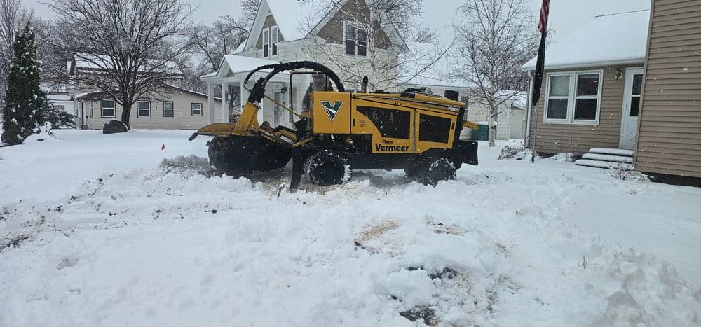 Vermeer snow plow clearing snow in residential area during winter storm.
