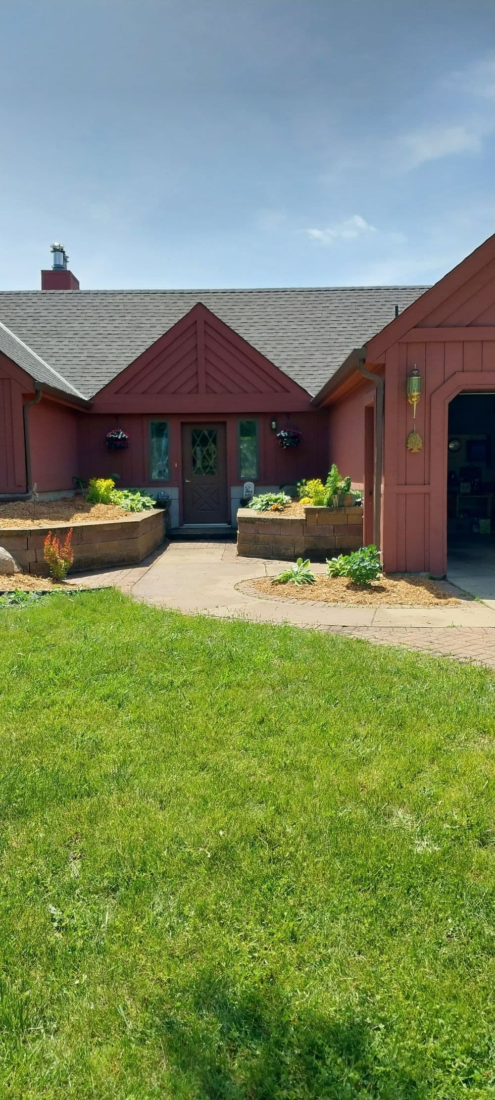 Charming red house with garden beds and stone walkway on a sunny day.