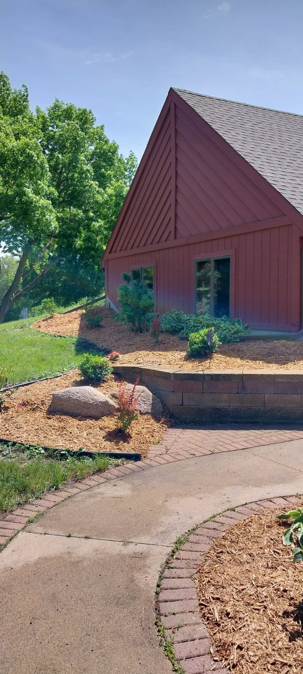 Red house with sloped roof, landscaped garden, and stone pathway in sunny outdoor setting.
