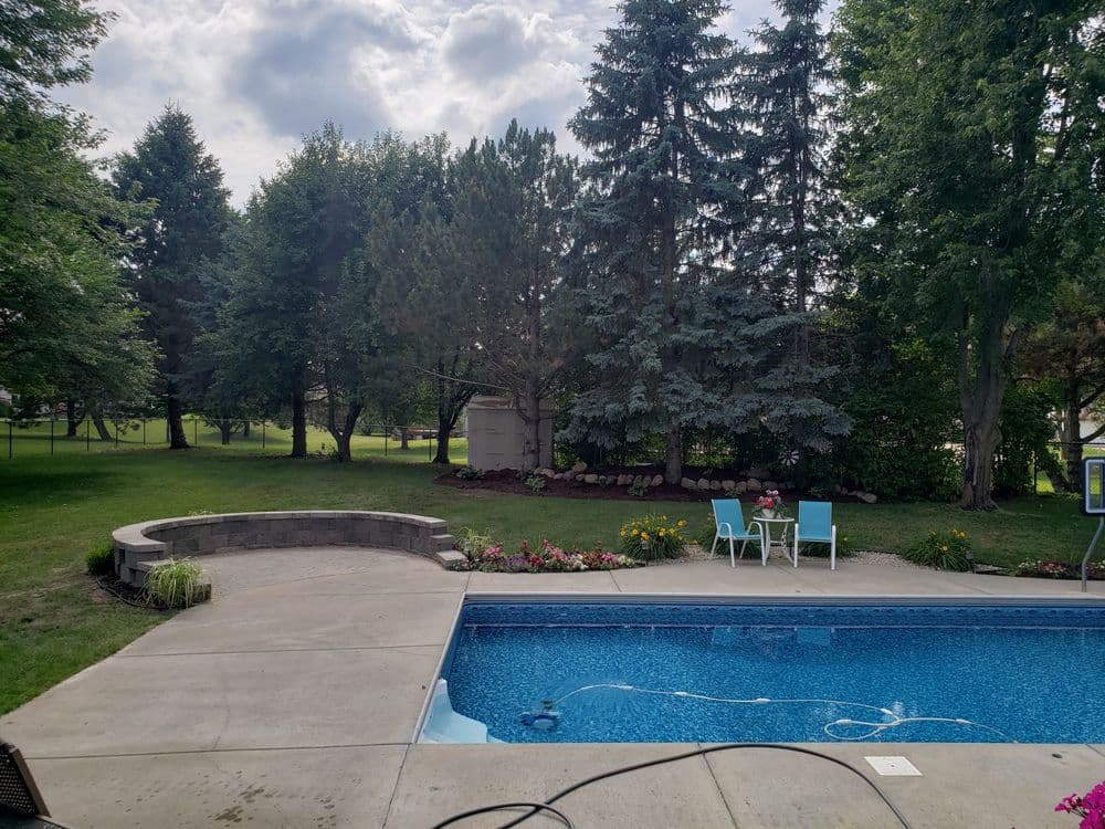 Backyard pool with seating area surrounded by lush greenery and flowers on a sunny day.