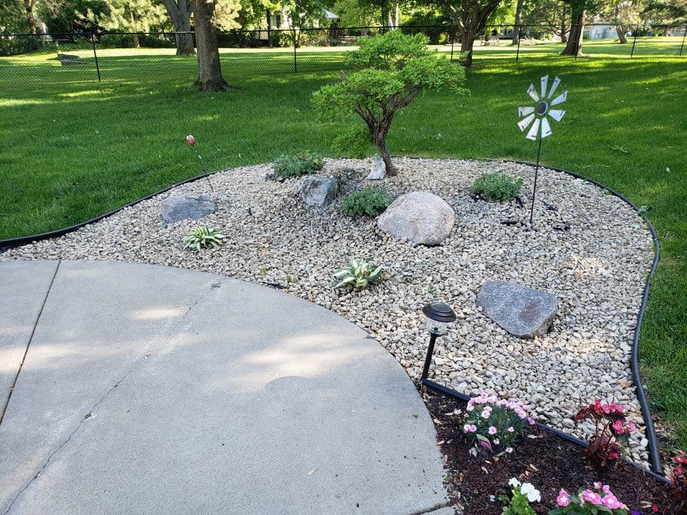 Zen garden with rocks, plants, and decorative wind spinner in a sunny green yard.