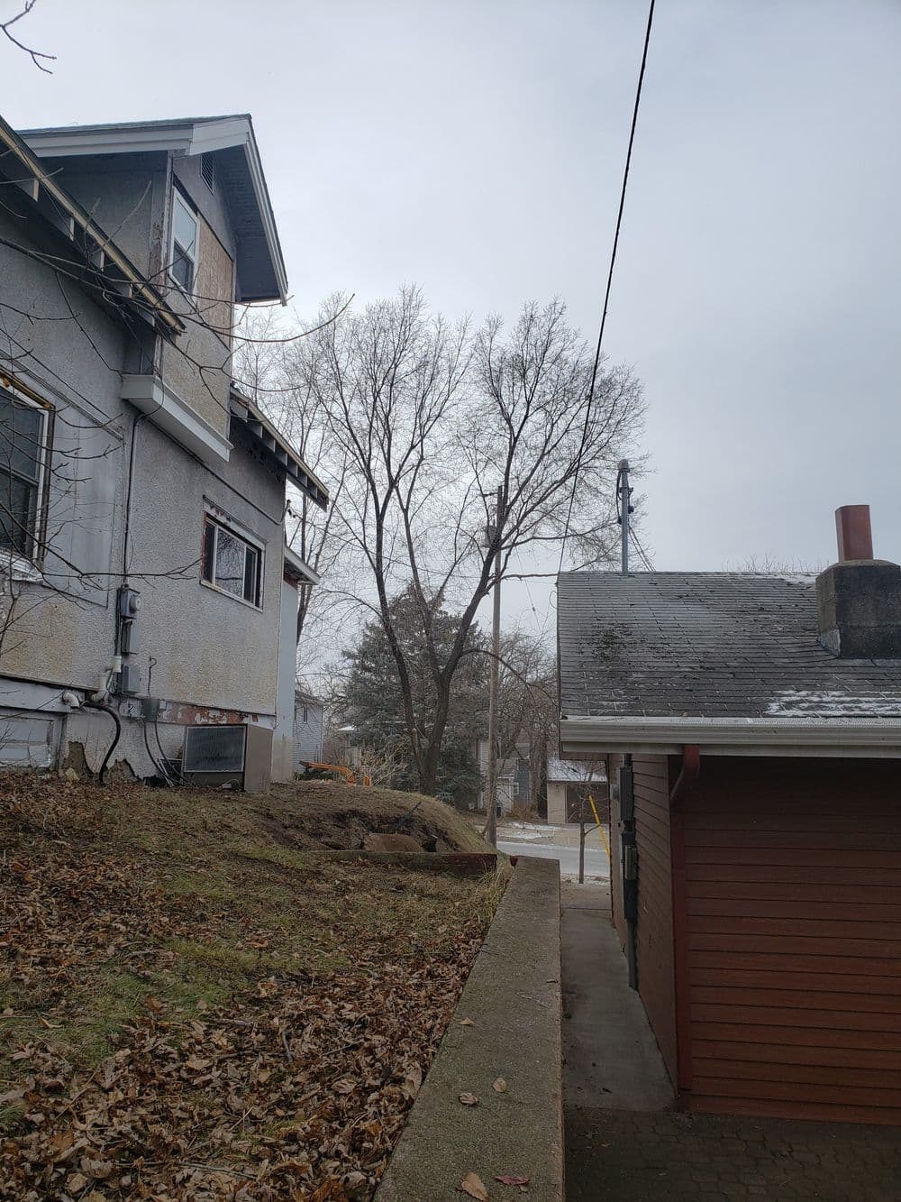 Side view of a house with bare trees and a cloudy sky in a residential area.