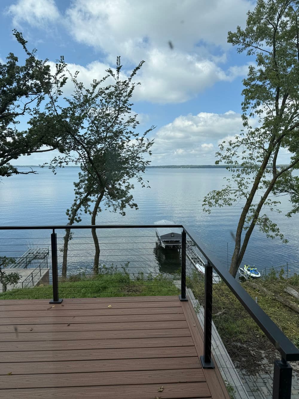 View of peaceful lake with trees and a dock, under a cloudy sky from a deck.