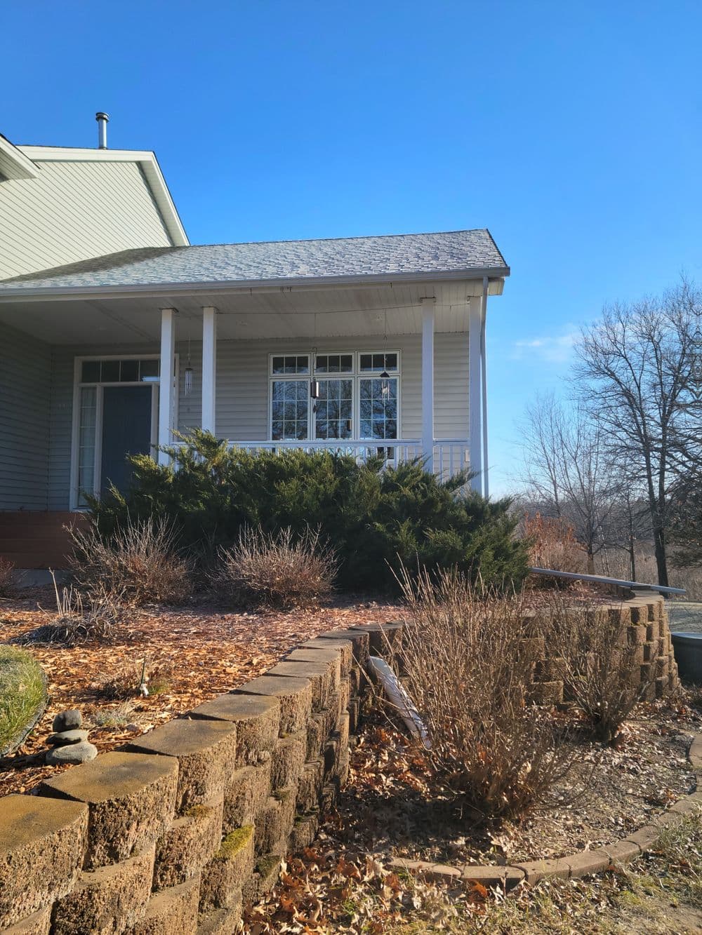 Front view of a modern house with a porch, landscaped garden, and clear blue sky.