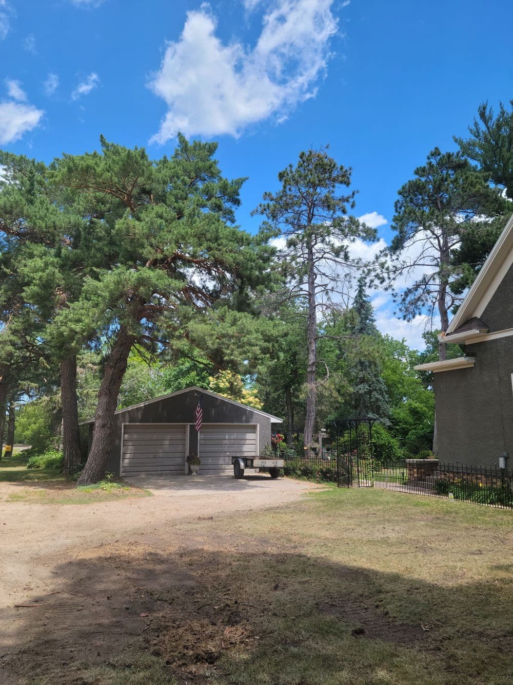 Gray garage with American flag surrounded by tall trees under a blue sky.